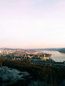 黄昏时分，港口城市的空中全景图美丽动人，柔和的夜空下可见起重机和海滨建筑