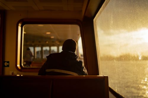 Free A solitary figure on a ferry gazes out at the sunset, capturing a tranquil and pensive atmosphere. Stock Photo