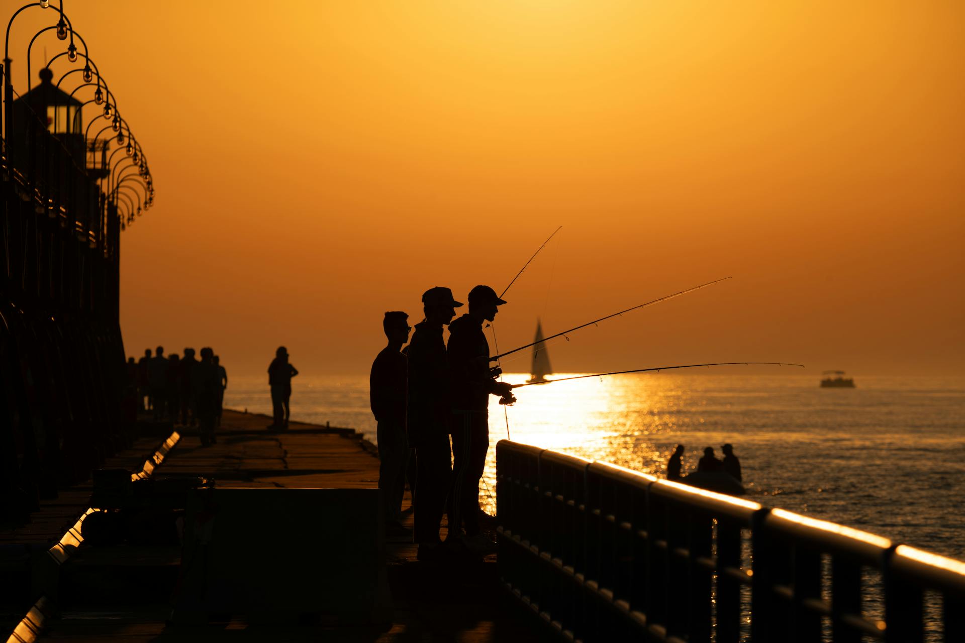 Fishermen silhouetted at sunset on Lake Michigan pier. A serene, warm evening scene.