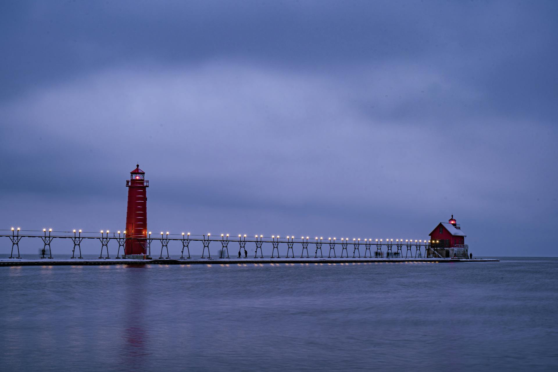 A serene winter evening view of a lighthouse on Lake Michigan with a calm blue sky.