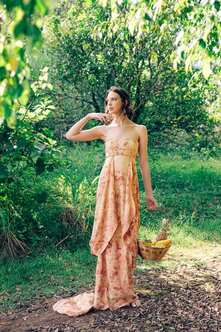 Woman in a floral dress holding a basket in a lush garden setting.