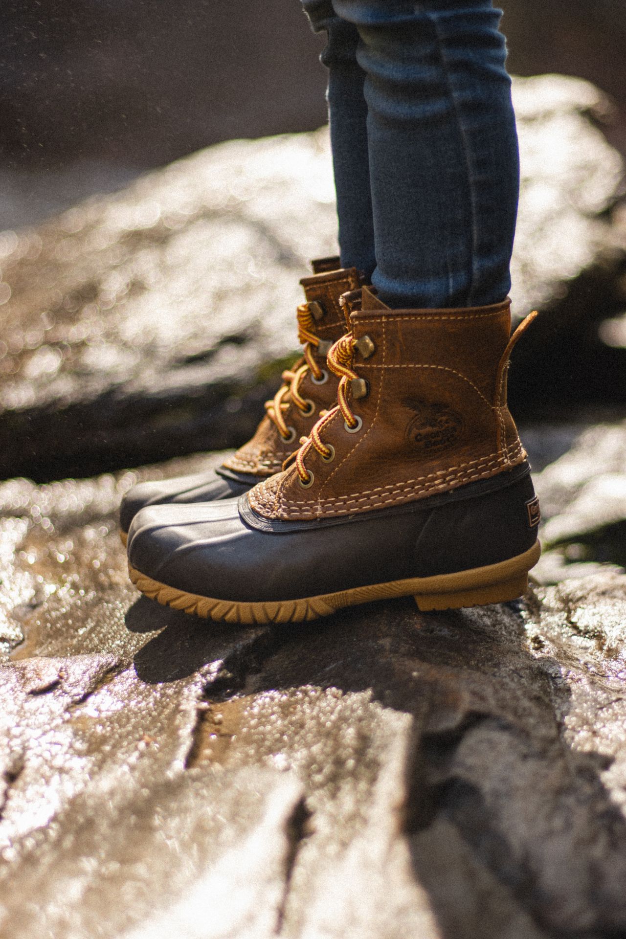 Insulated duck boots with jeans on wet rocks