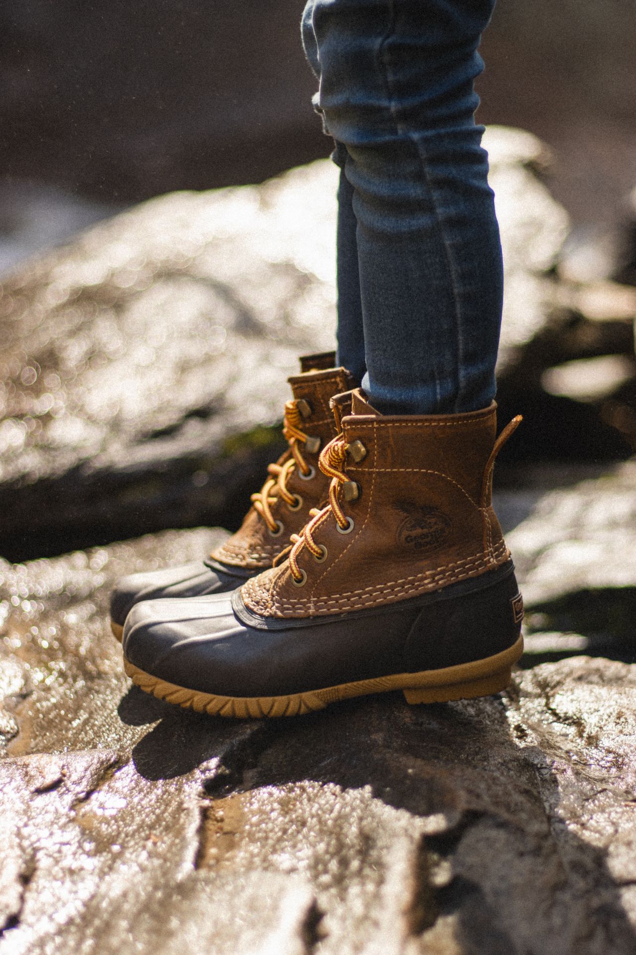 Child's feet in lace-up duck boots standing on wet rocks