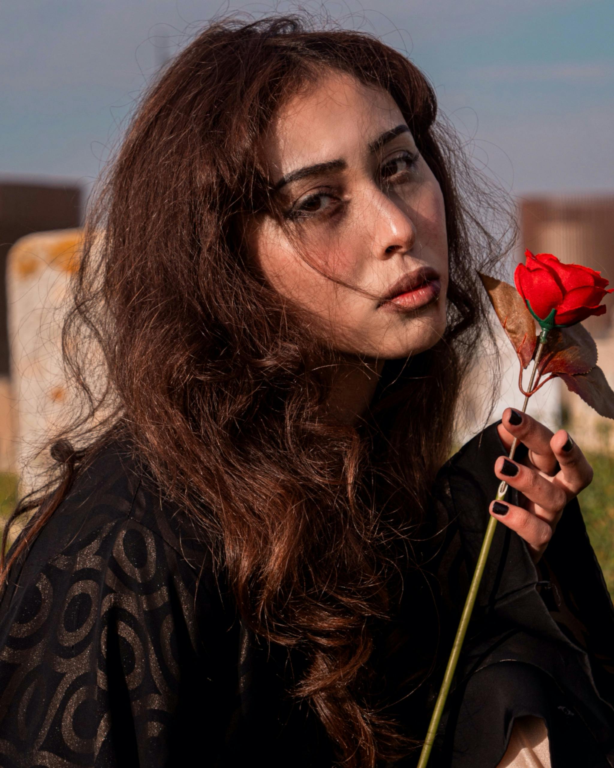 Artistic portrait of a woman with flowing hair holding a red rose outdoors.