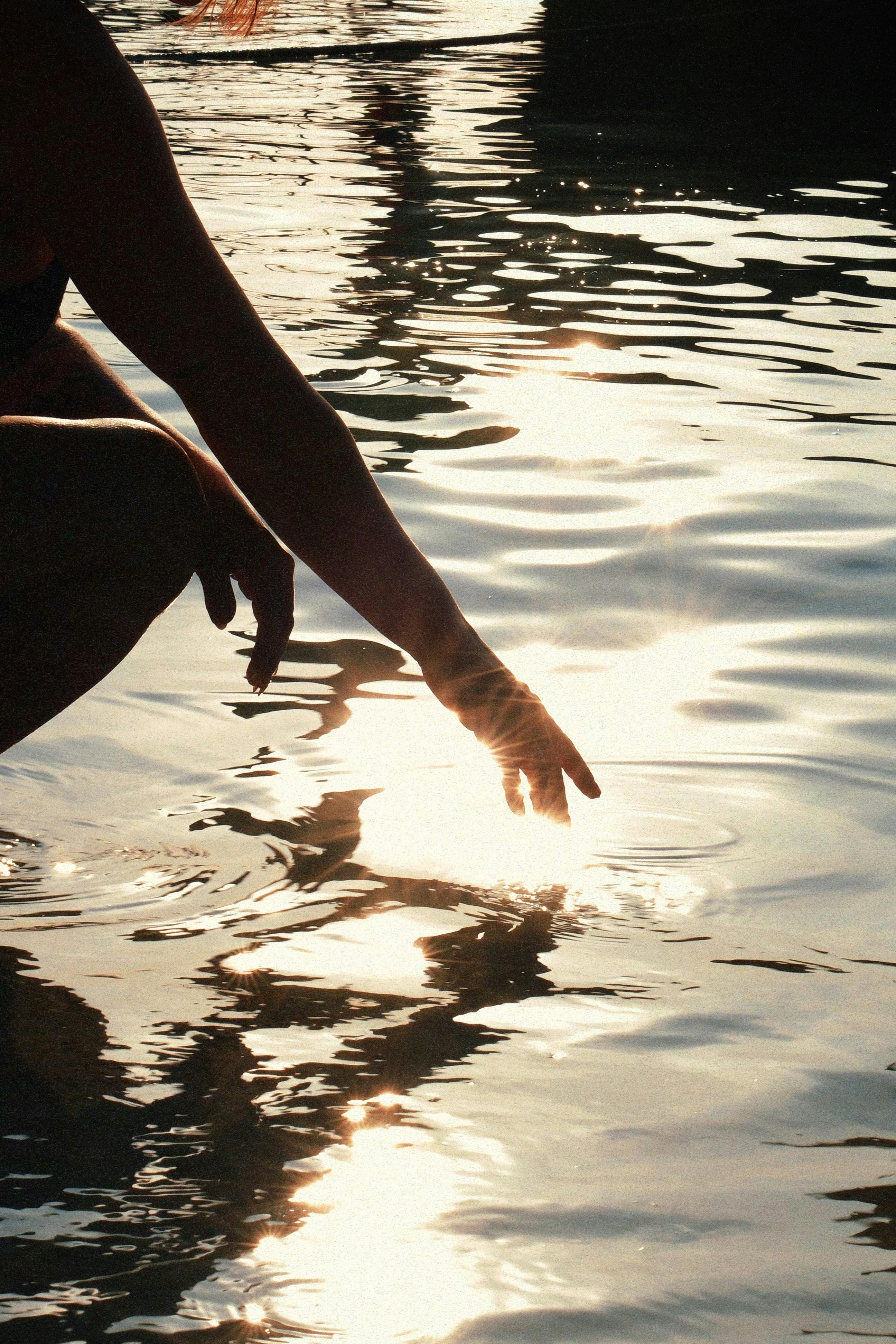 A serene silhouette of a hand touching sunlit water in Satun, Thailand, capturing a tranquil moment.