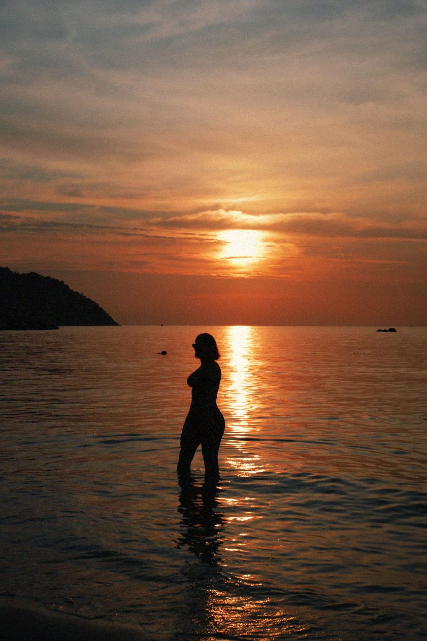 De silhouet van een vrouw staat in kalm water bij zonsondergang in Satun, Thailand.