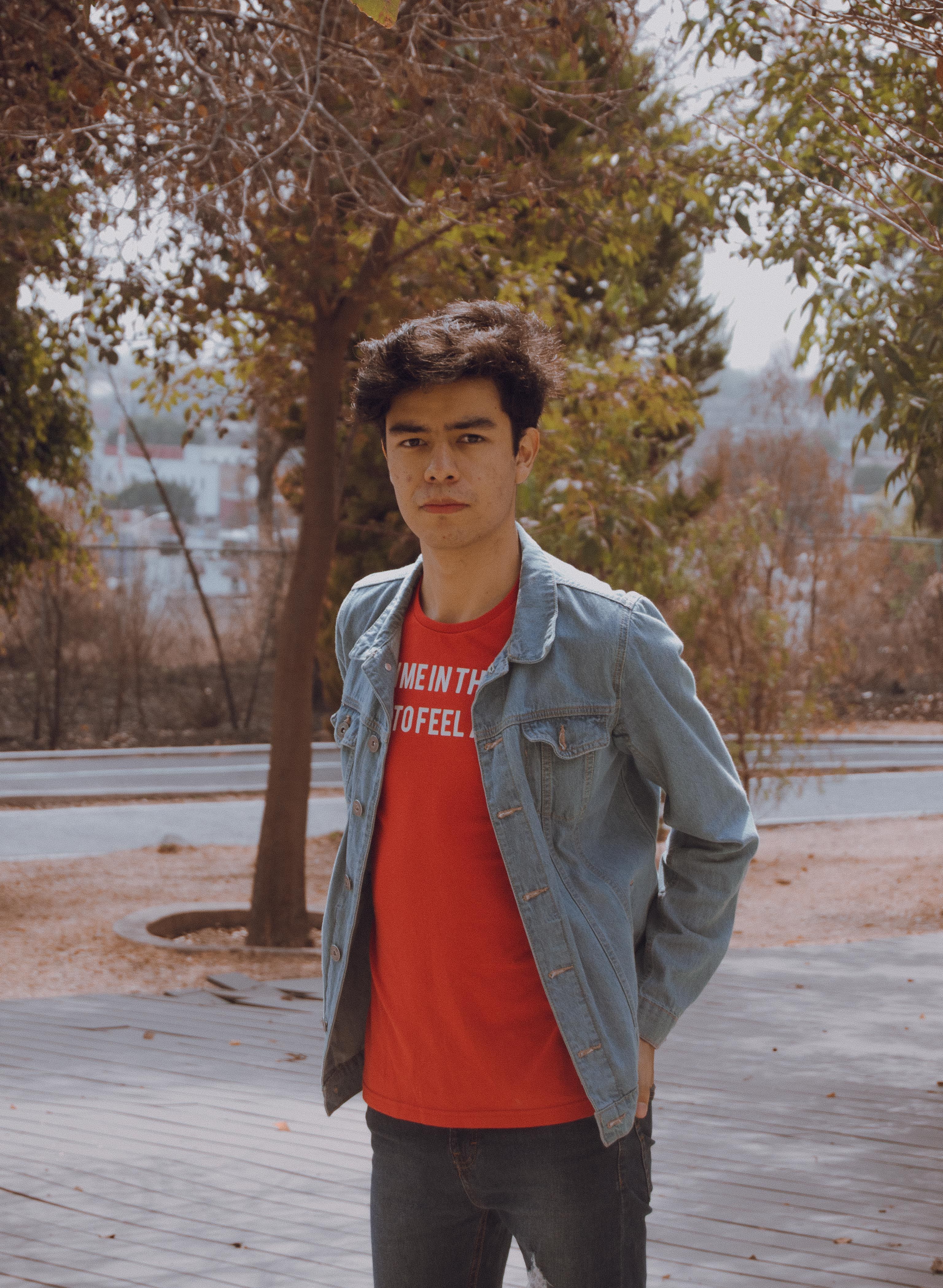 Portrait of a young man wearing a denim jacket and red shirt outdoors in autumn.