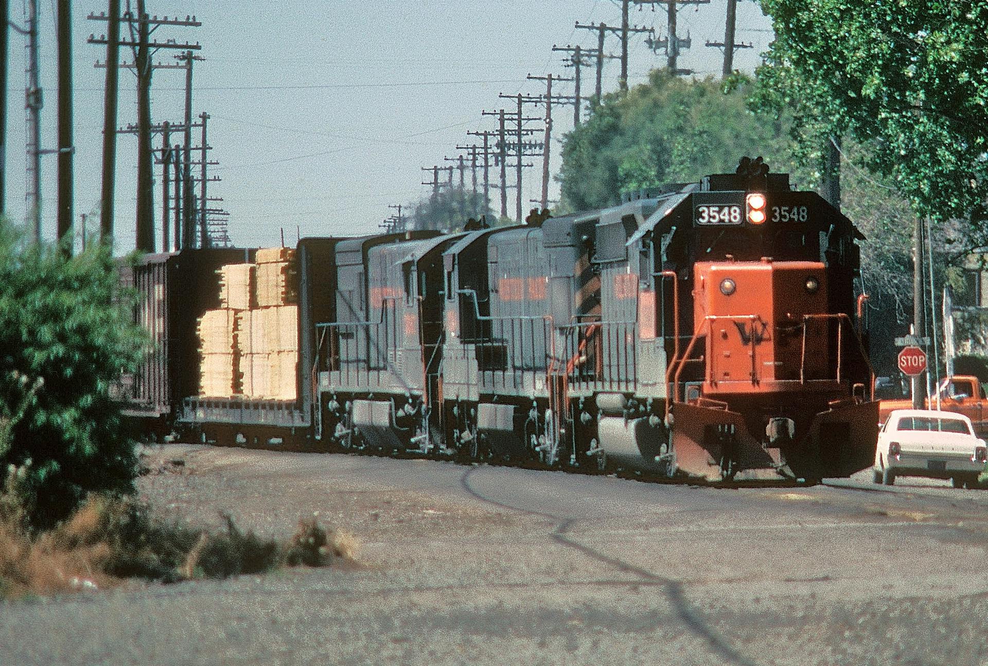 A freight train carrying lumber travels through Stockton, California in daylight.