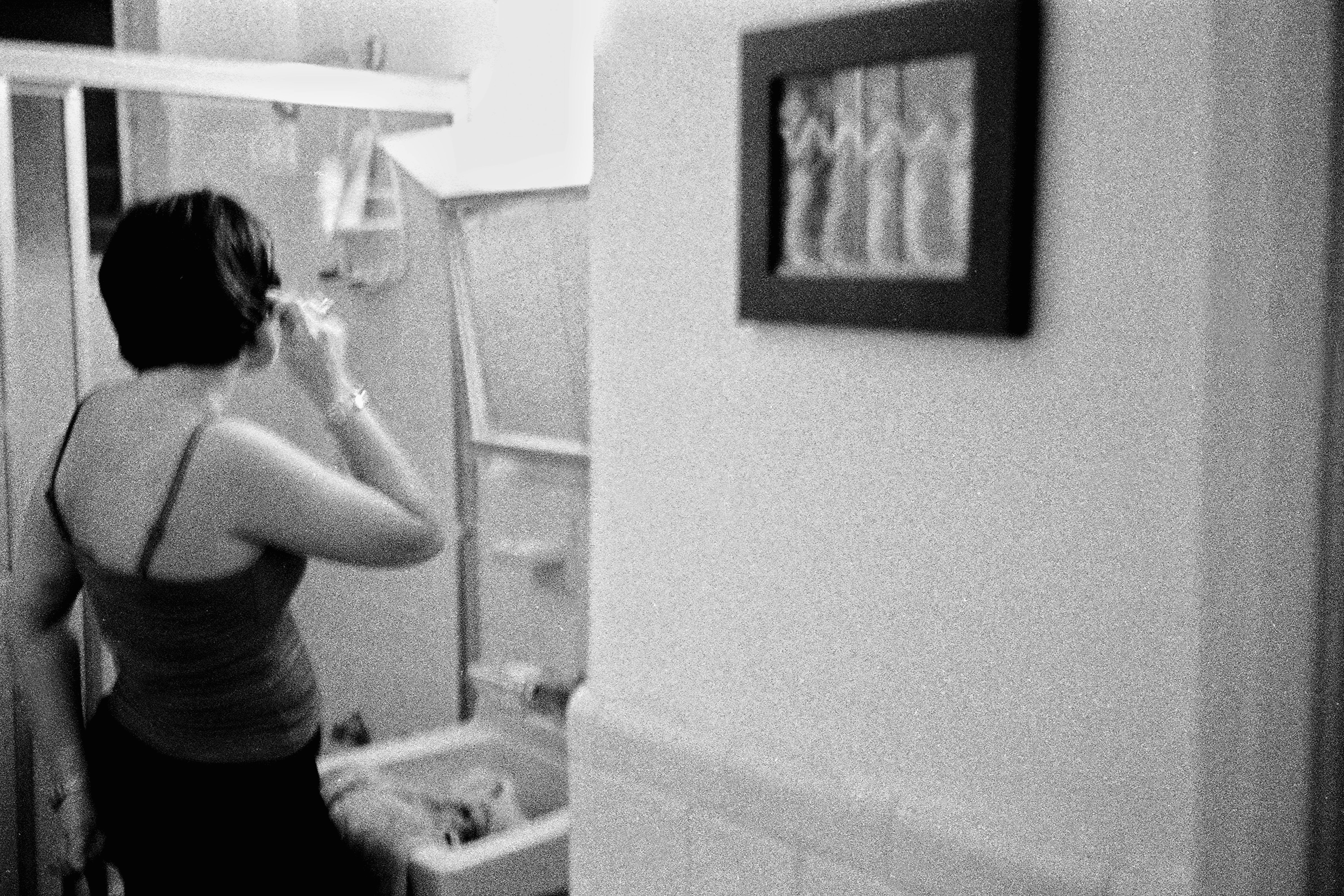 A woman adjusts her hair in a dimly lit indoor setting, captured in black and white.