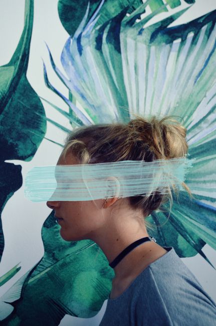 Profile of a woman with paint stroke over eyes, against a leafy background.
