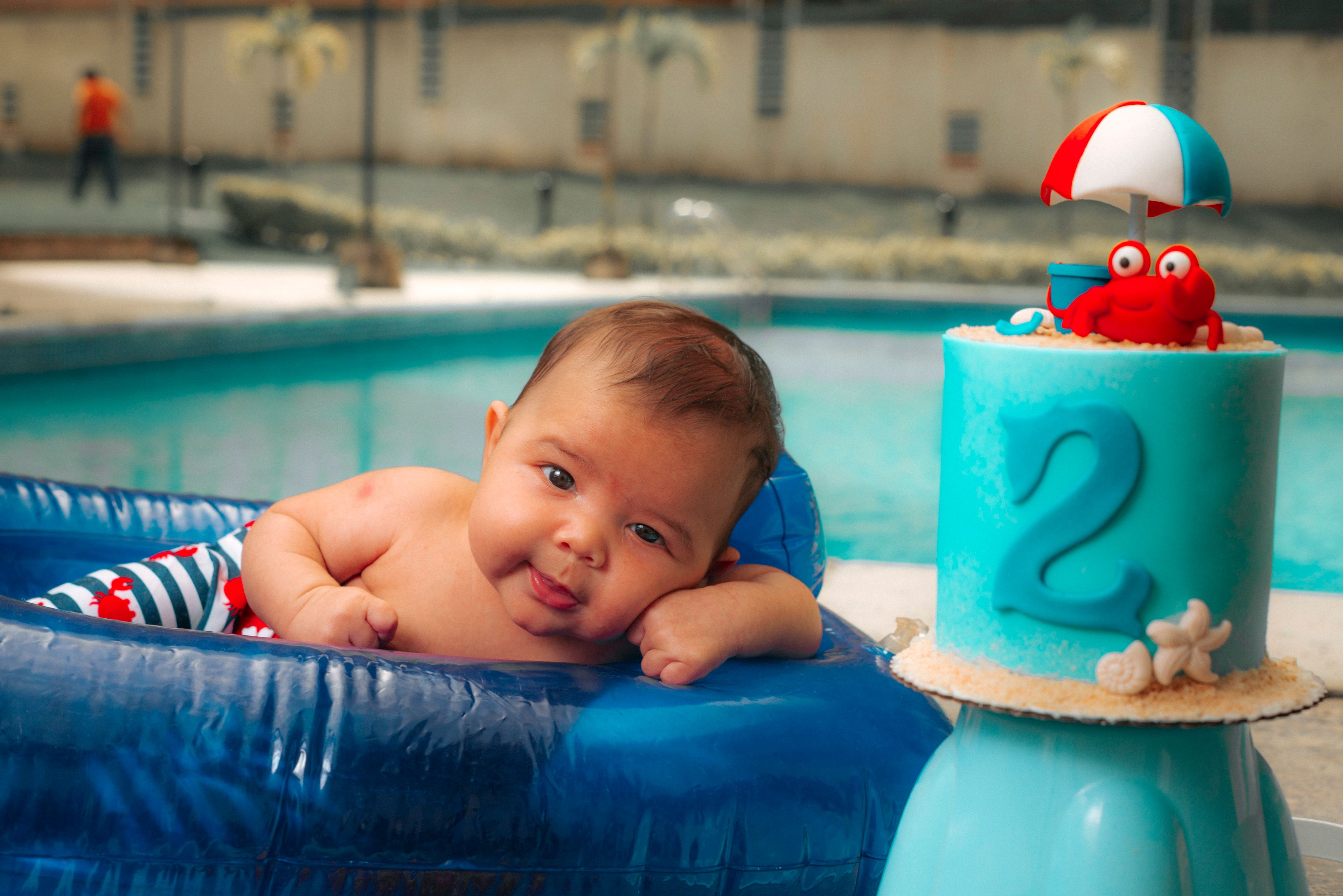 Cute baby enjoying pool time next to a vibrant birthday cake with a crab design.