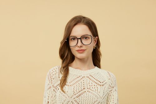 Free Portrait of a woman in chic glasses and knit sweater against a neutral background. Stock Photo
