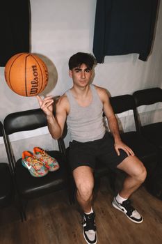 Young athlete spinning basketball in locker room with sneakers and chairs.