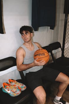 Young man in casual sportswear holding a basketball indoors, sitting on a chair.