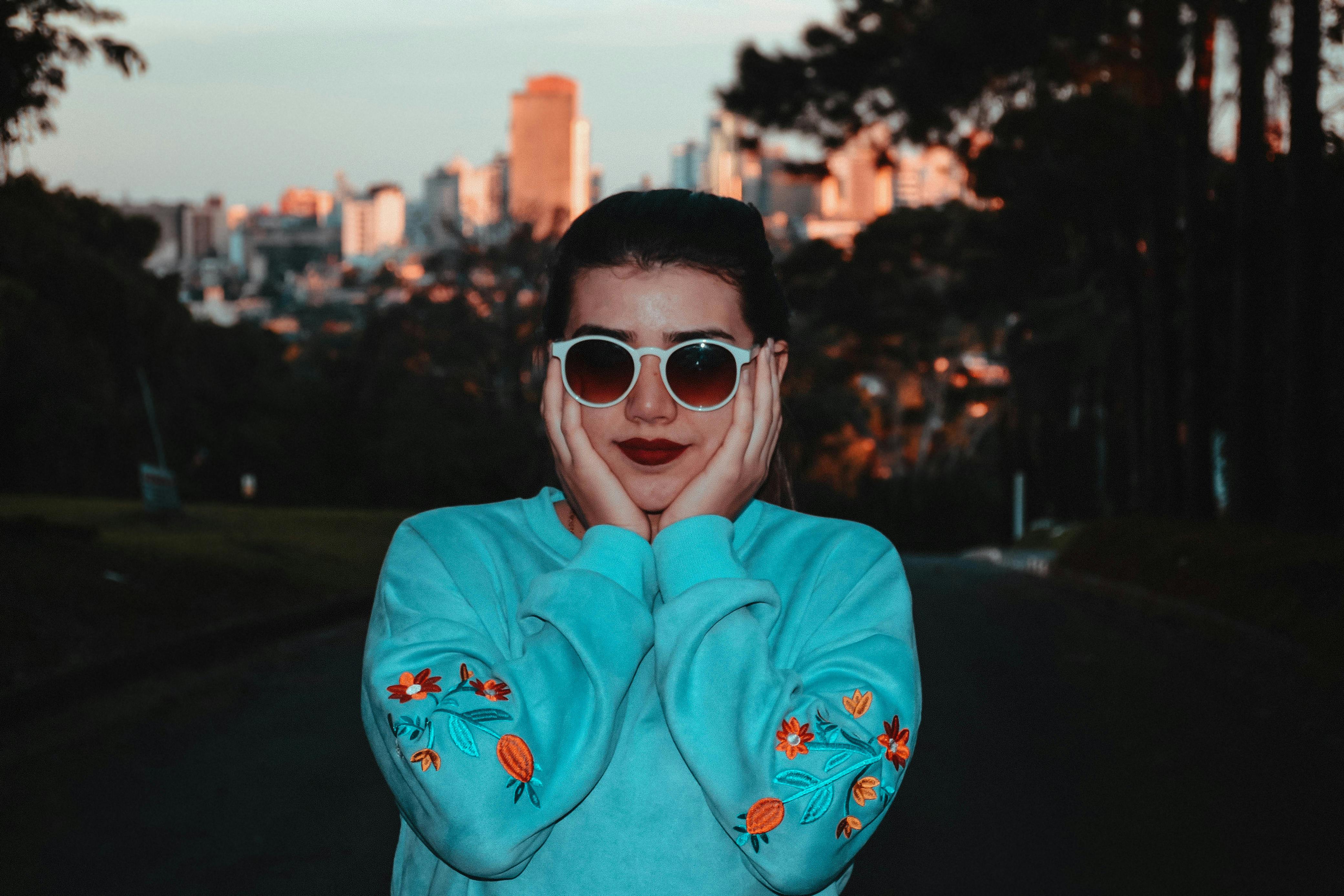 日落时分，一位戴着太阳镜的时尚女士在户外摆姿势，背景是充满活力的城市景观