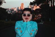日落时分，一位戴着太阳镜的时尚女士在户外摆姿势，背景是充满活力的城市景观