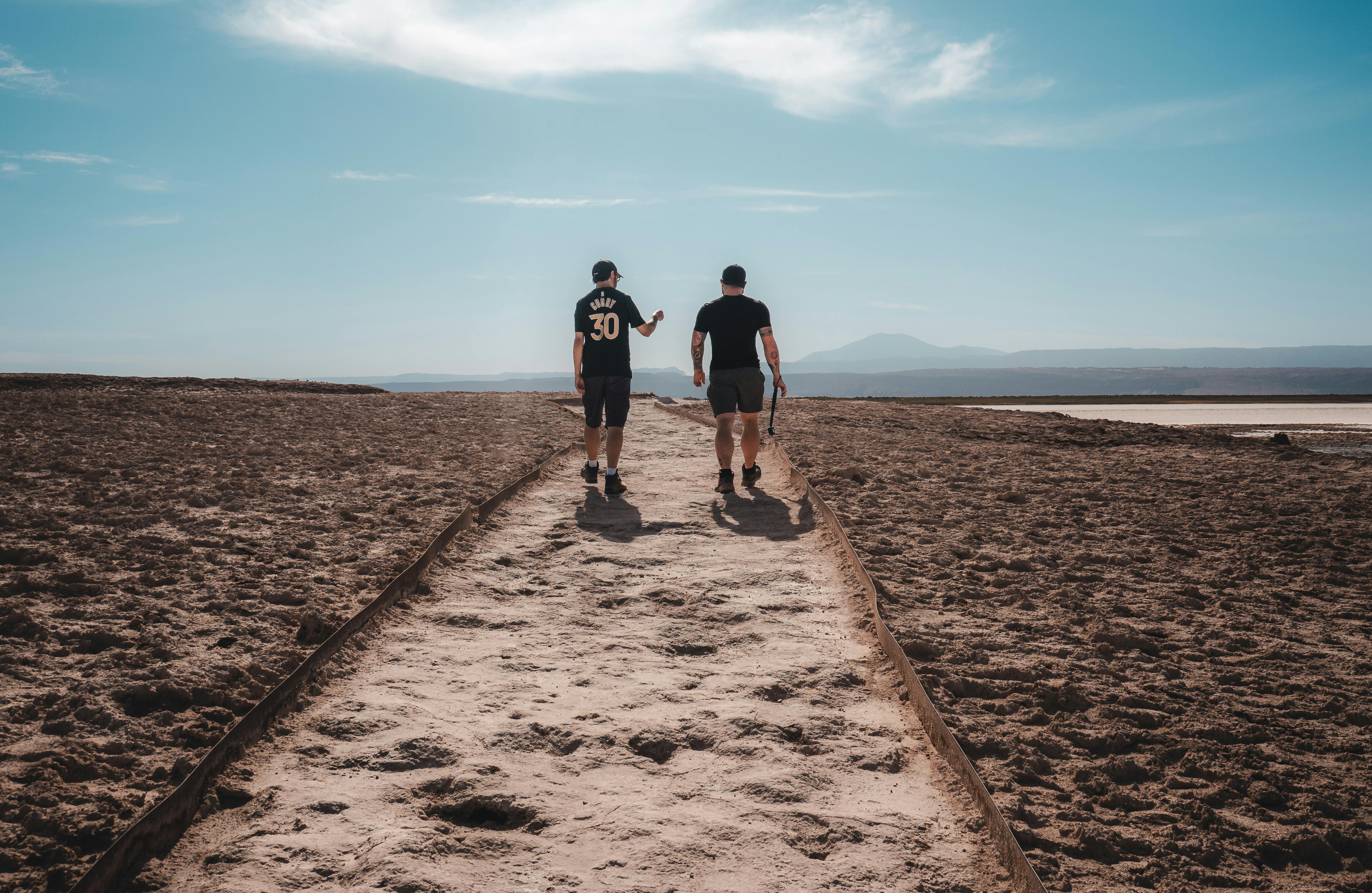 Two men walking along a sandy path in the vast Atacama Desert, Chile, under a clear sky.