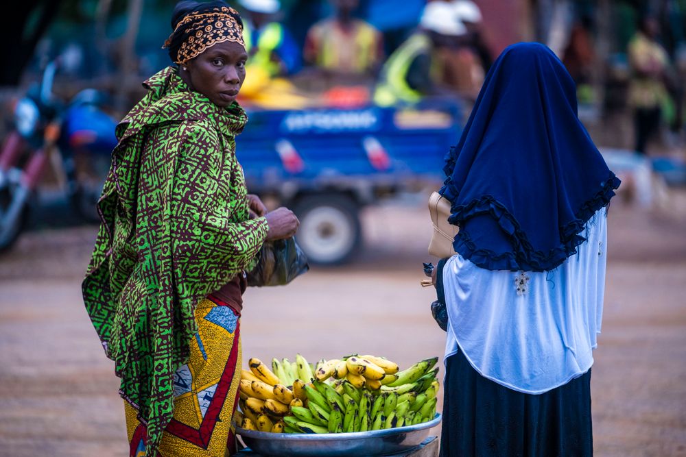 Two women in traditional attire trading bananas at a busy market