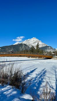 Stunning winter scene with snow-covered mountain and bridge under a clear blue sky.