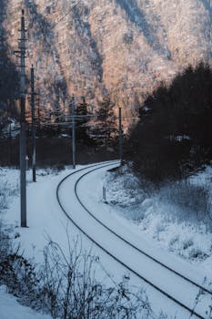 Serene railway tracks winding through a snowy mountainous landscape under clear winter skies.
