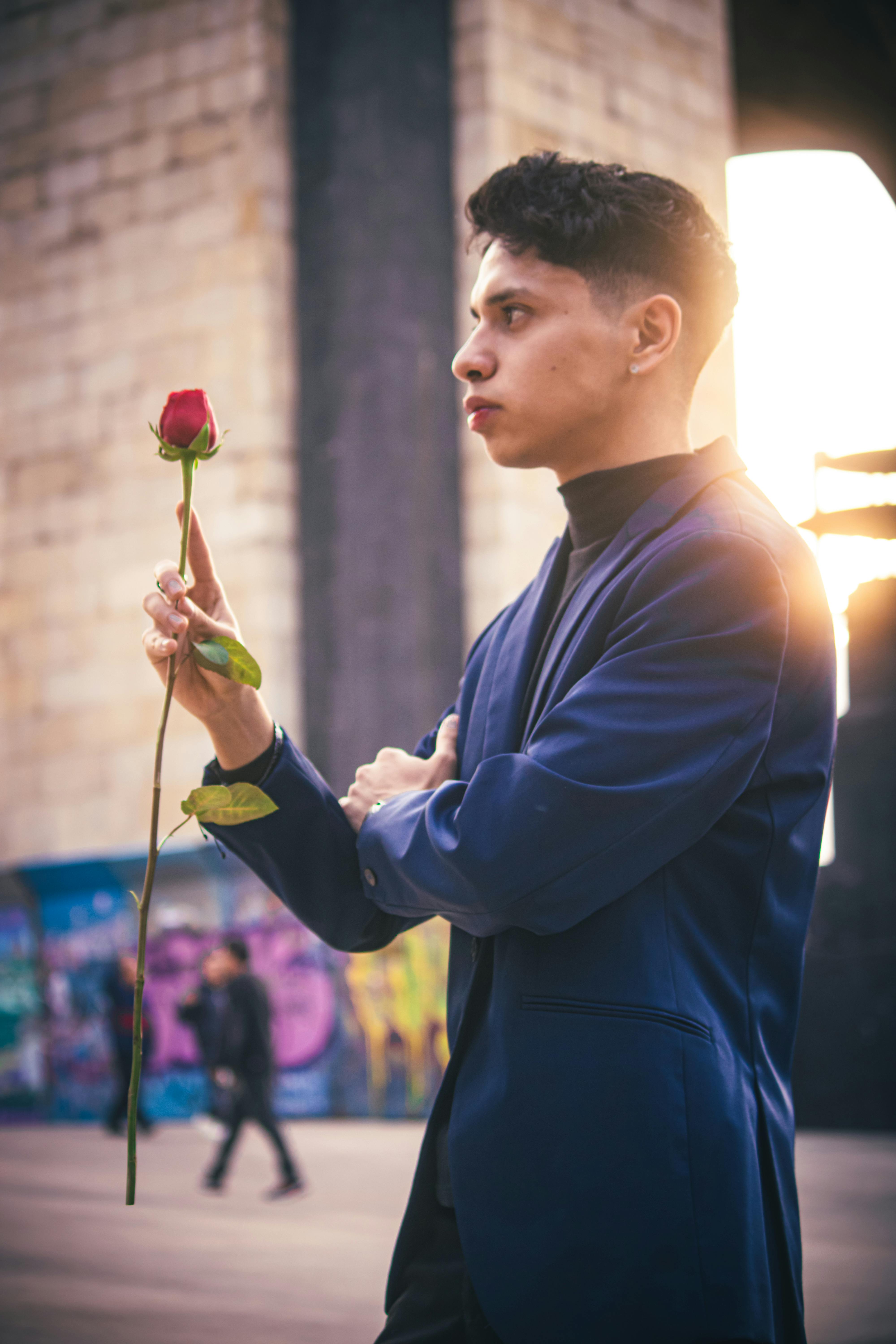 Elegant man holding a red rose amidst a vibrant urban backdrop at sunset in Ciudad de México.