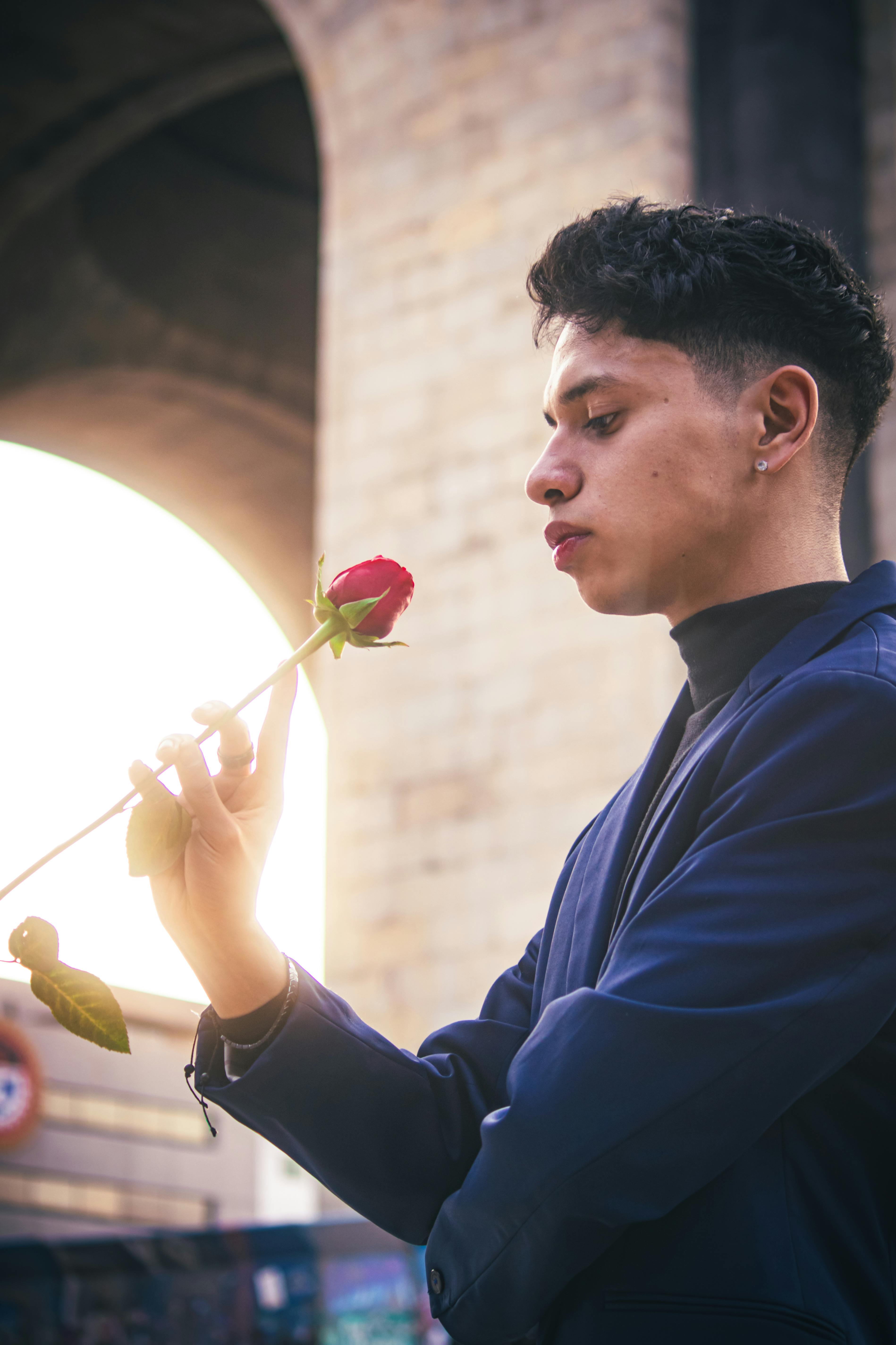 Young man in blue suit admiring a red rose outdoors during sunset in Ciudad de México.