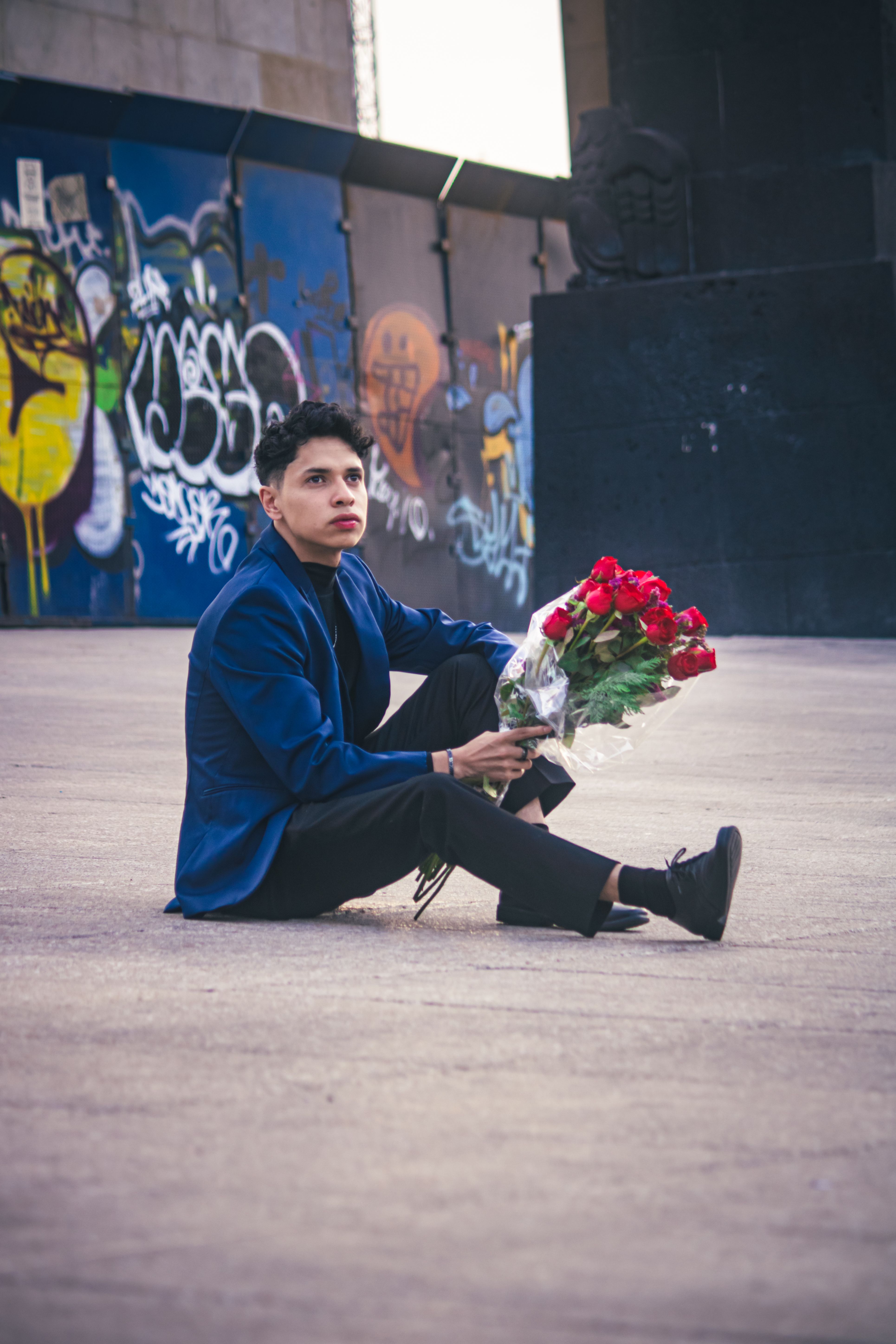A young man sits with roses against a graffiti backdrop, exuding a vibrant urban vibe.