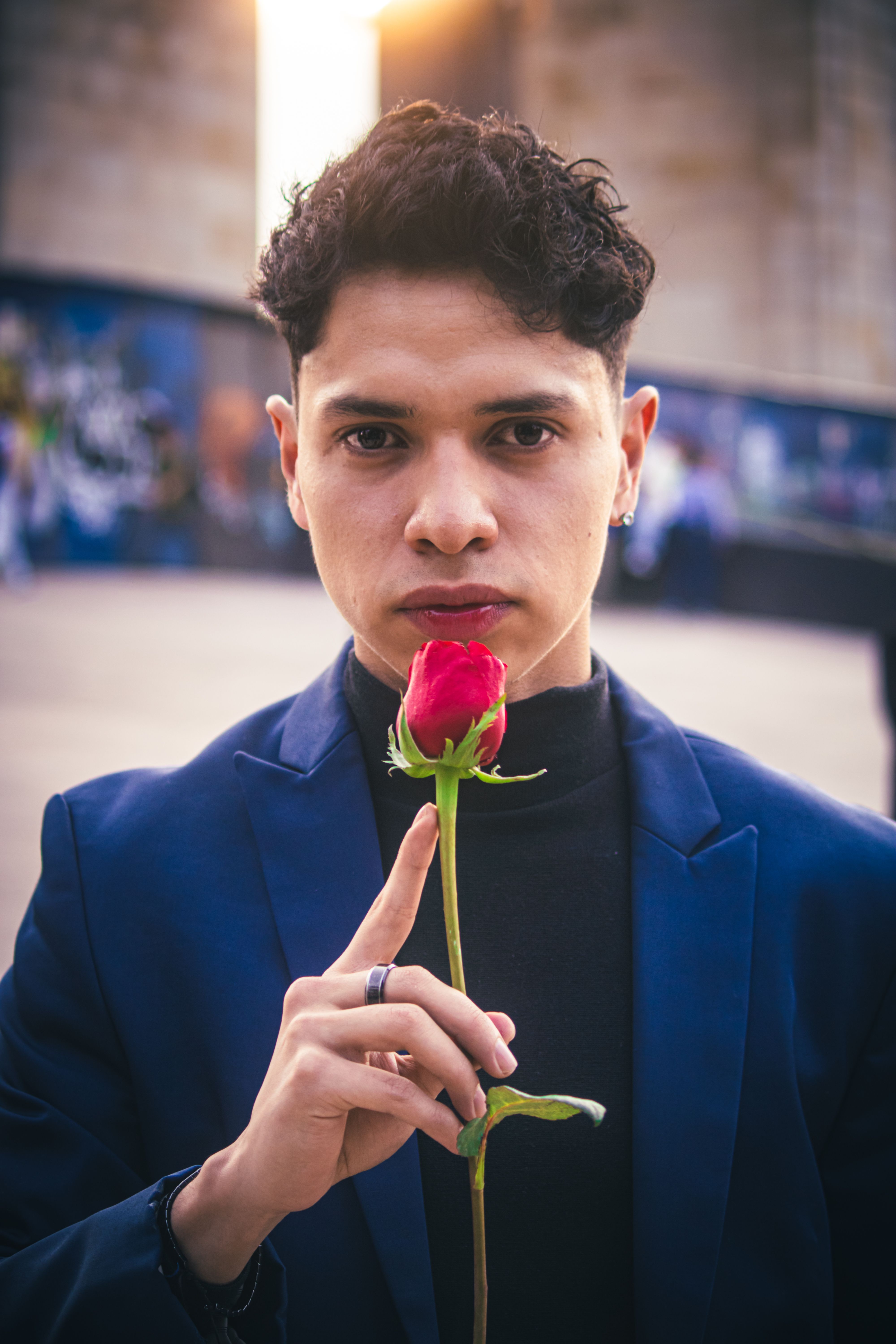 A man holding a red rose poses elegantly in Mexico City at sunset, radiating romance.