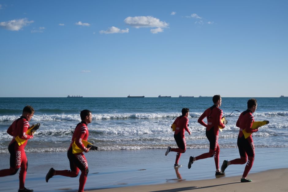 Lifeguards in training run along the beach in Spain, emphasizing teamwork and fitness.