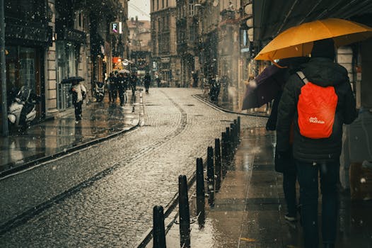 People with umbrellas walking on a rainy cobblestone street in an urban setting, creating a cozy and moody atmosphere.