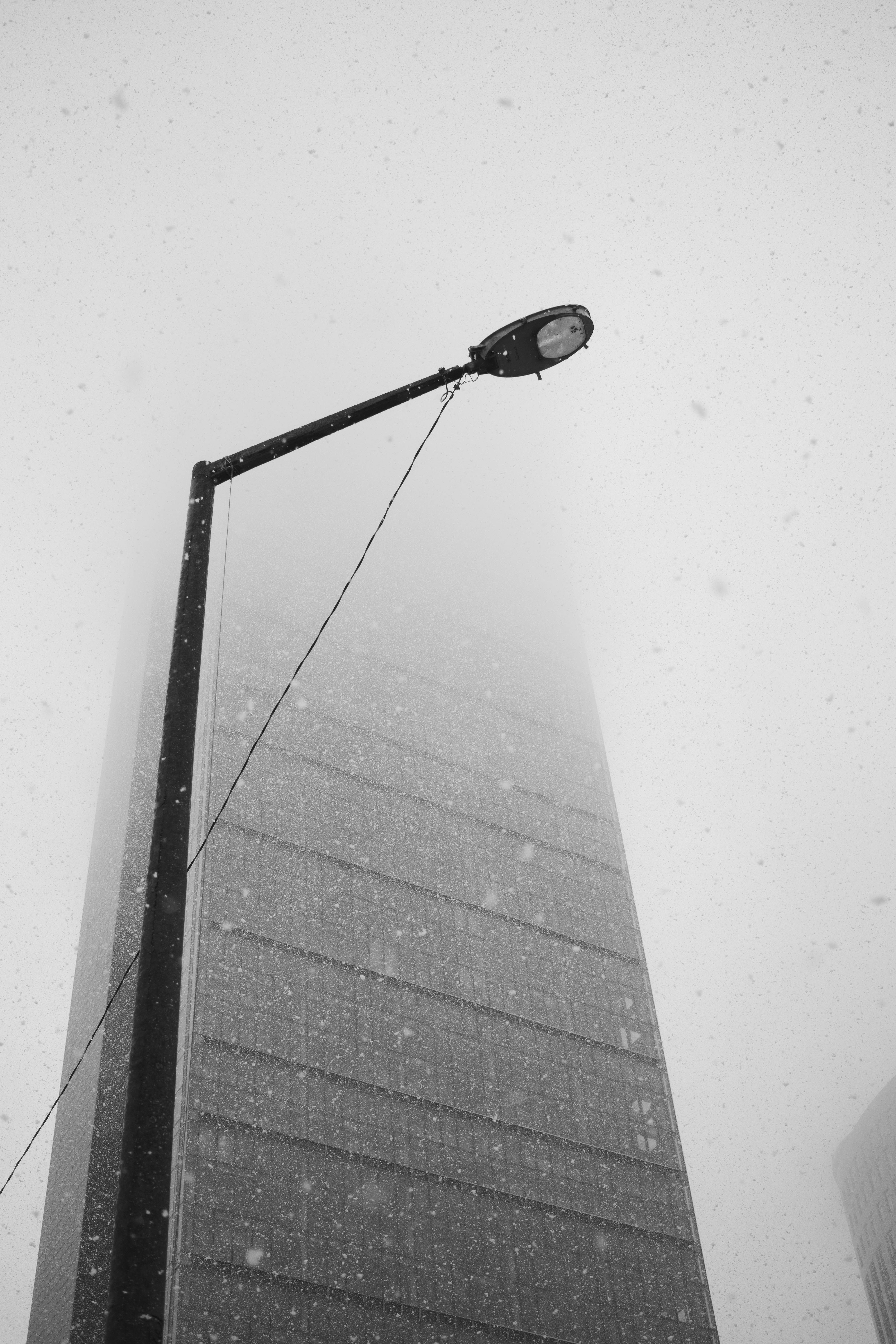 Black and white photo of a skyscraper disappearing into fog and snow, with a streetlight visible.