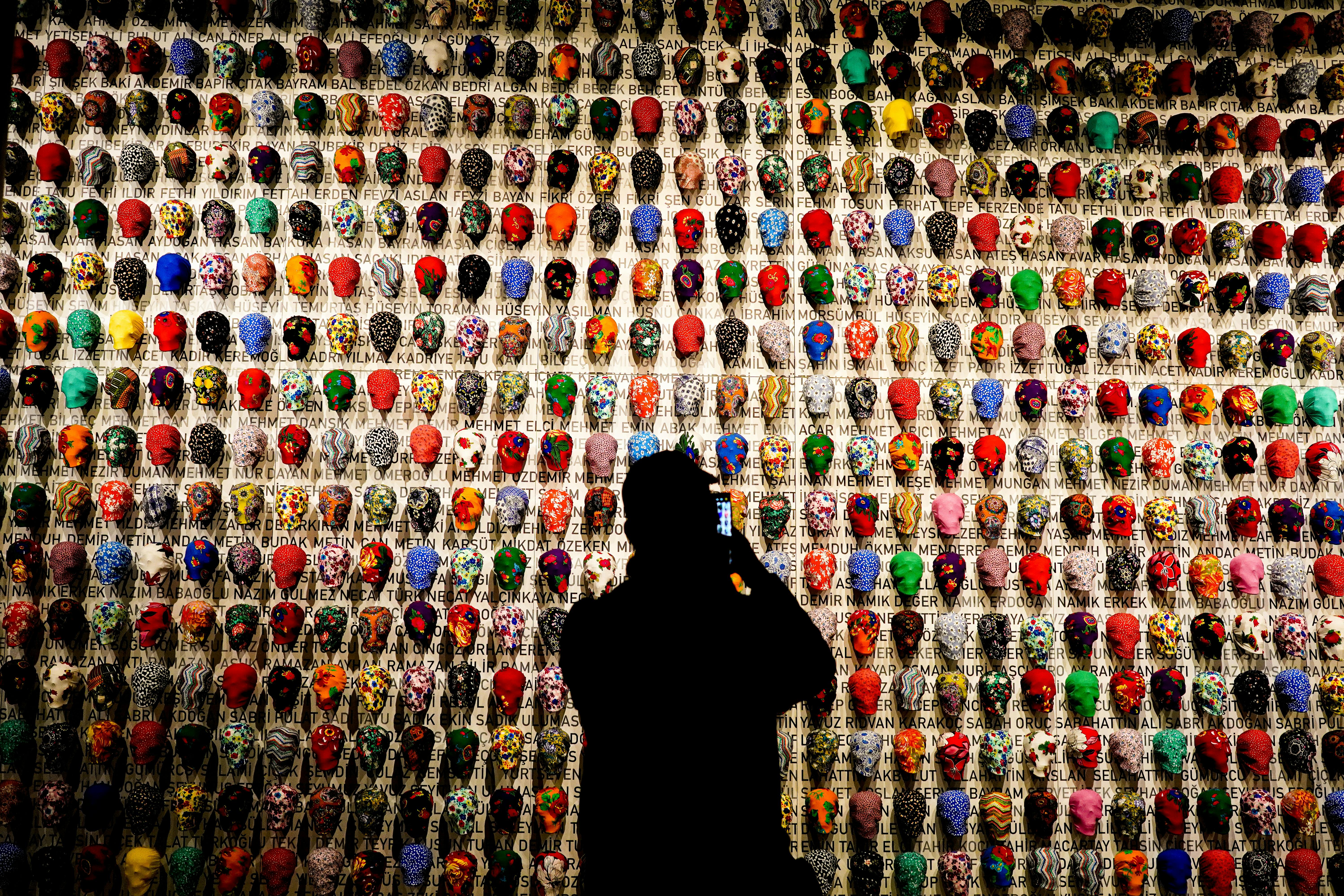 A silhouette photographs a colorful skull art installation with diverse patterns.