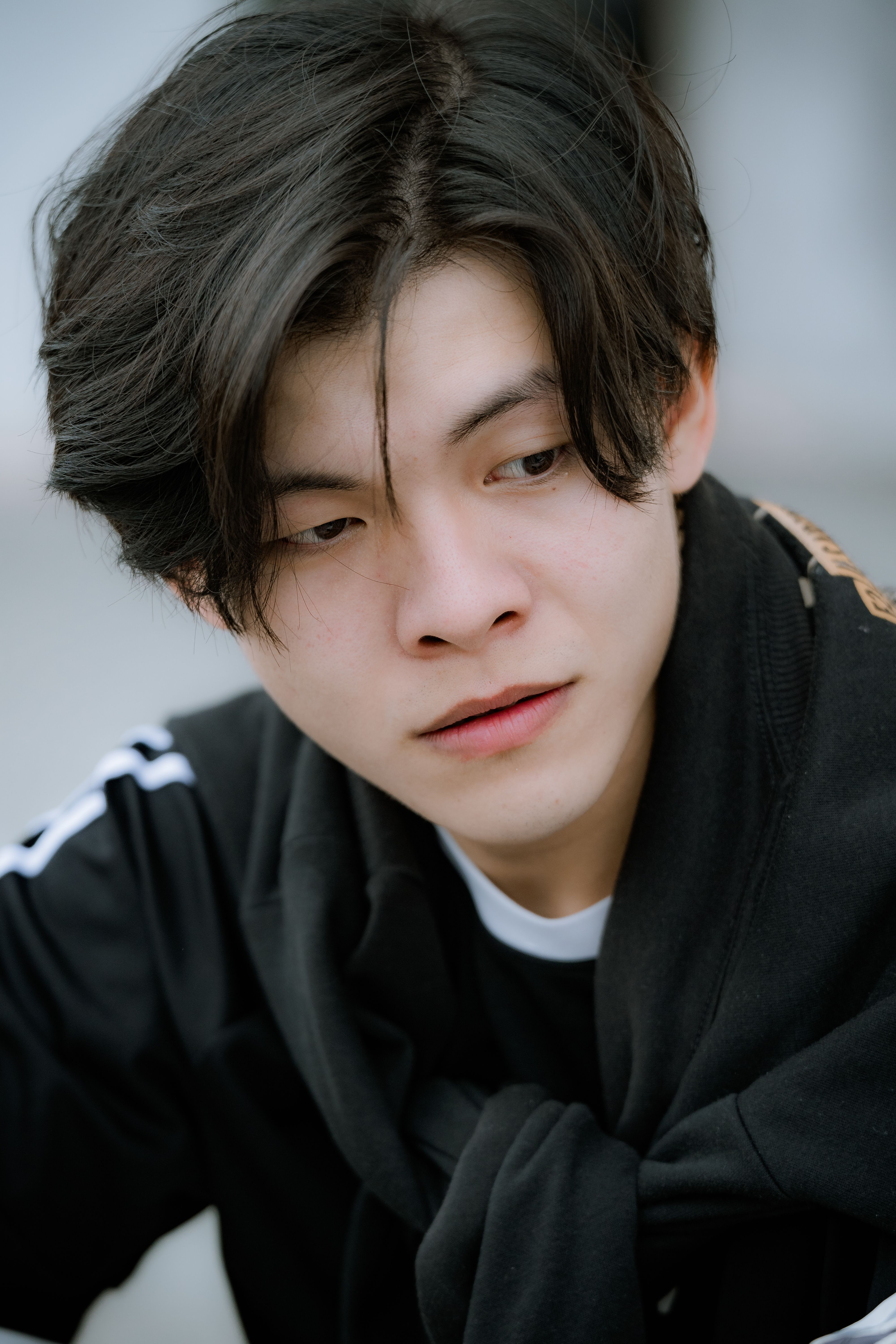 Portrait of a young man with black hair wearing a black jacket, looking thoughtful.