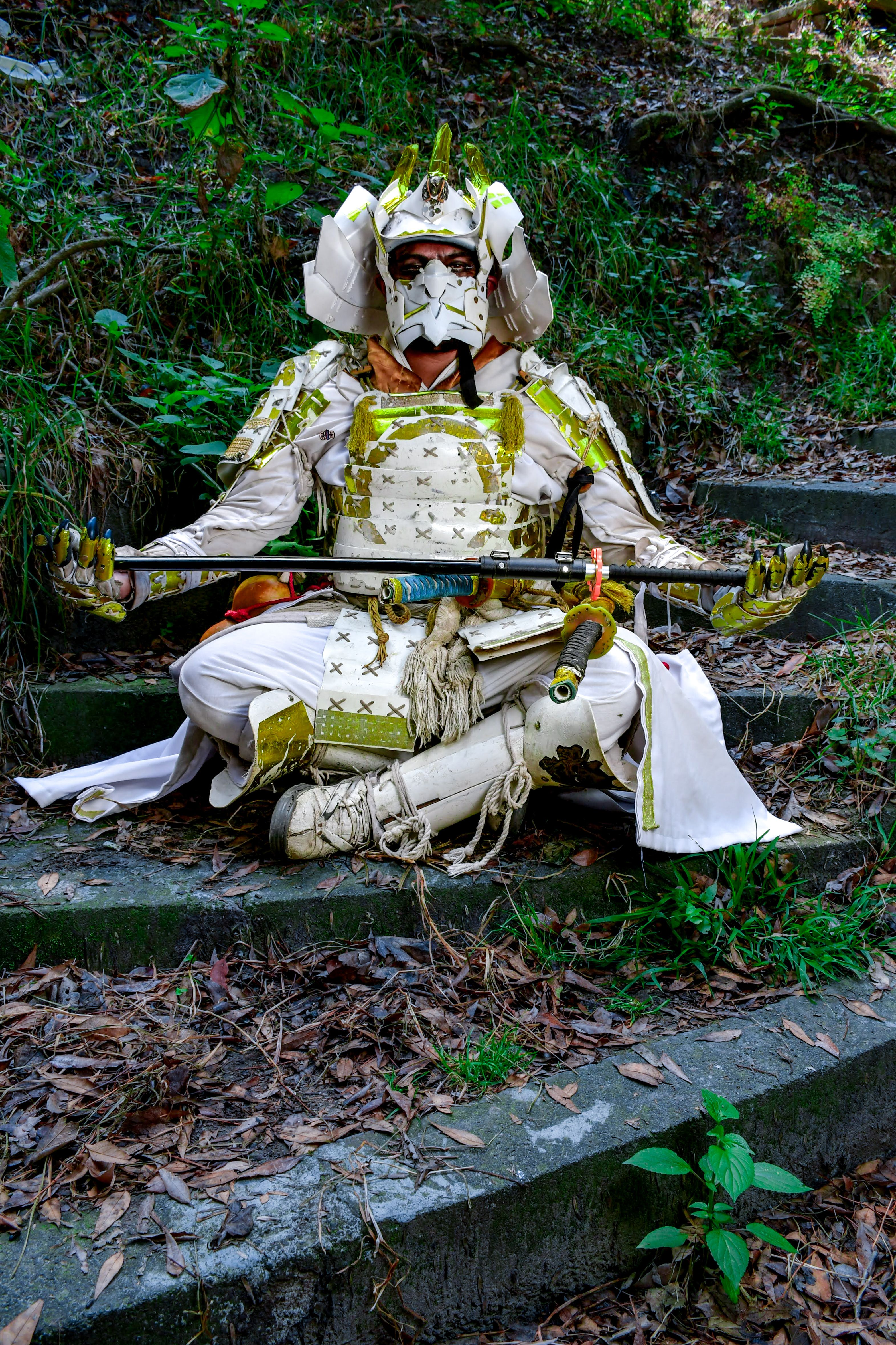A person in intricate samurai armor meditates outdoors, surrounded by nature.