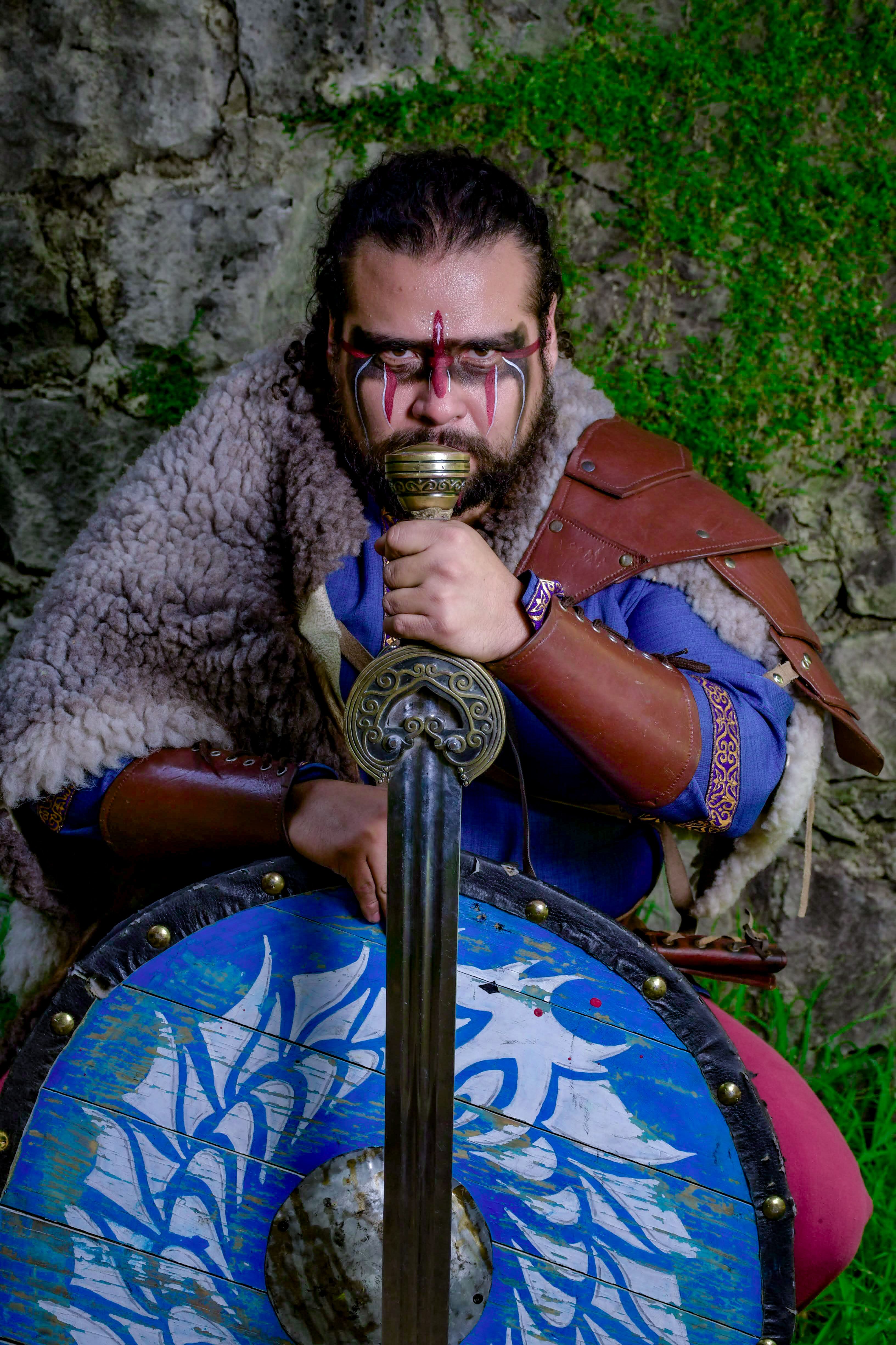 A medieval warrior with face paint holds a sword and shield, exuding strength.