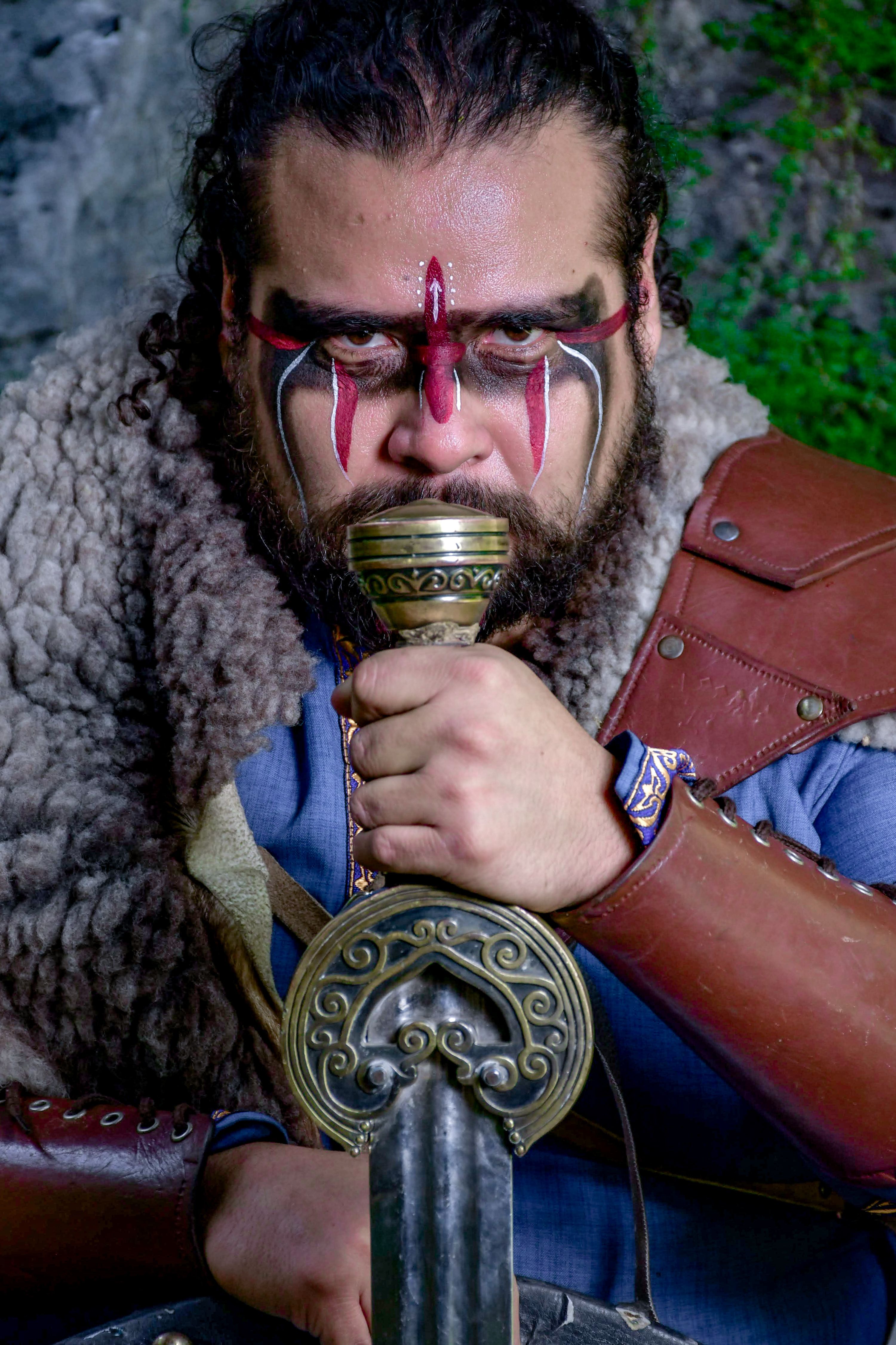 Medieval warrior with tribal face paint holding a decorated sword.