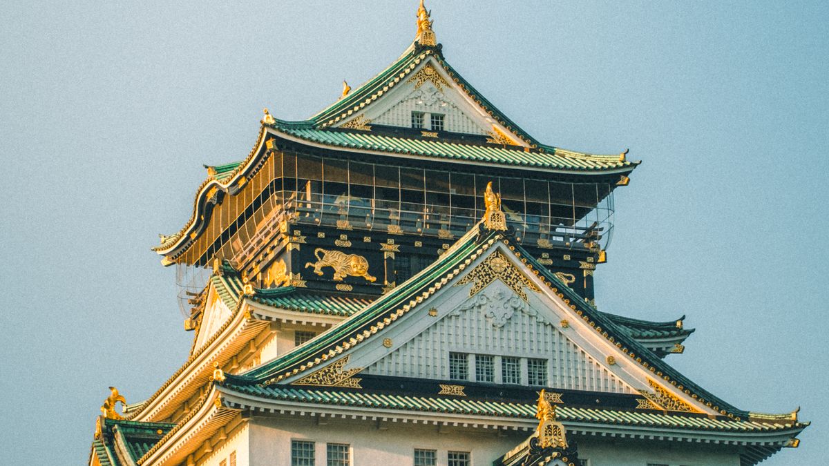 Osaka Castle main keep surrounded by green trees under a clear blue sky