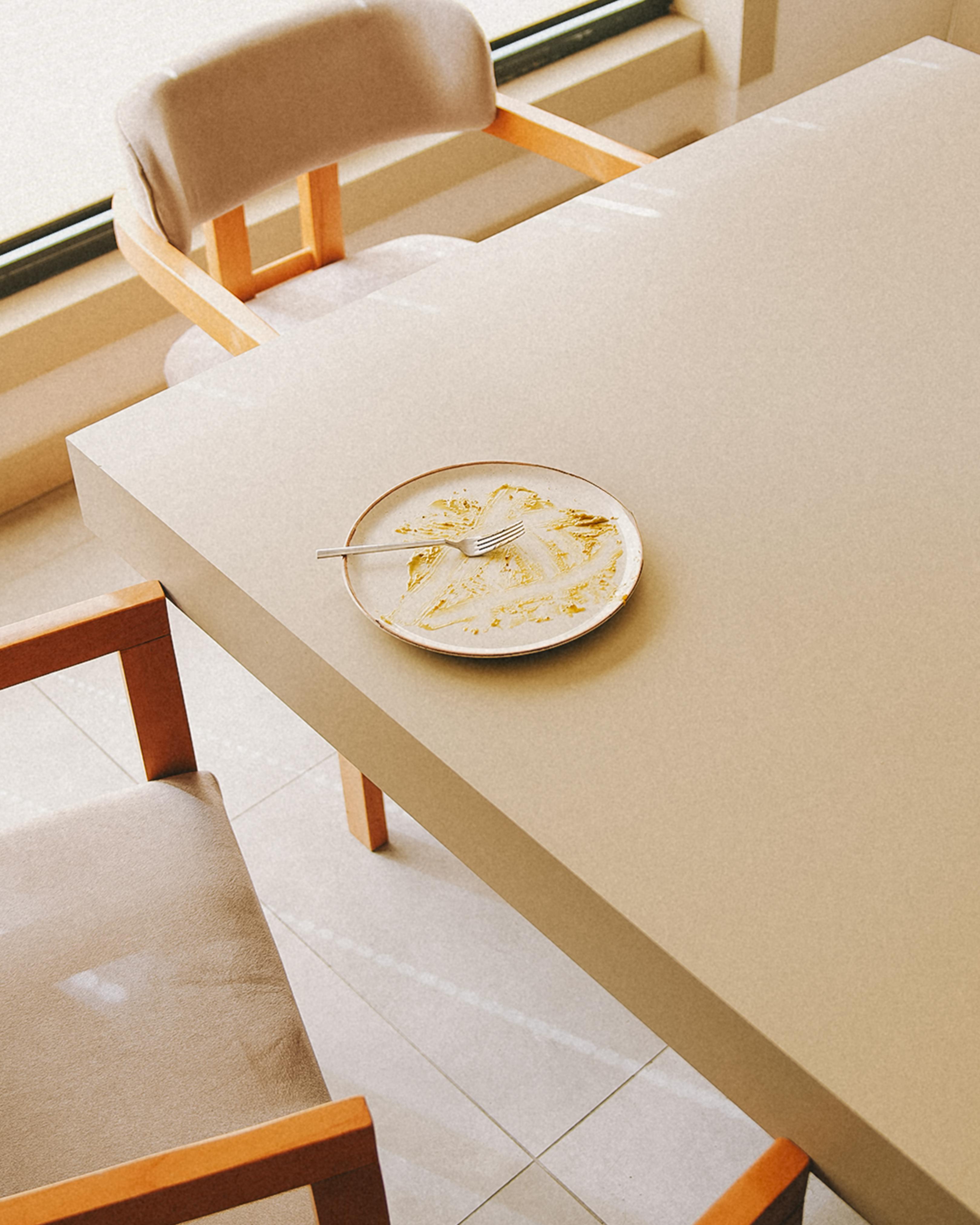 A minimalist indoor setting featuring a wooden table, chairs, and a white plate with a fork in Türkiye.