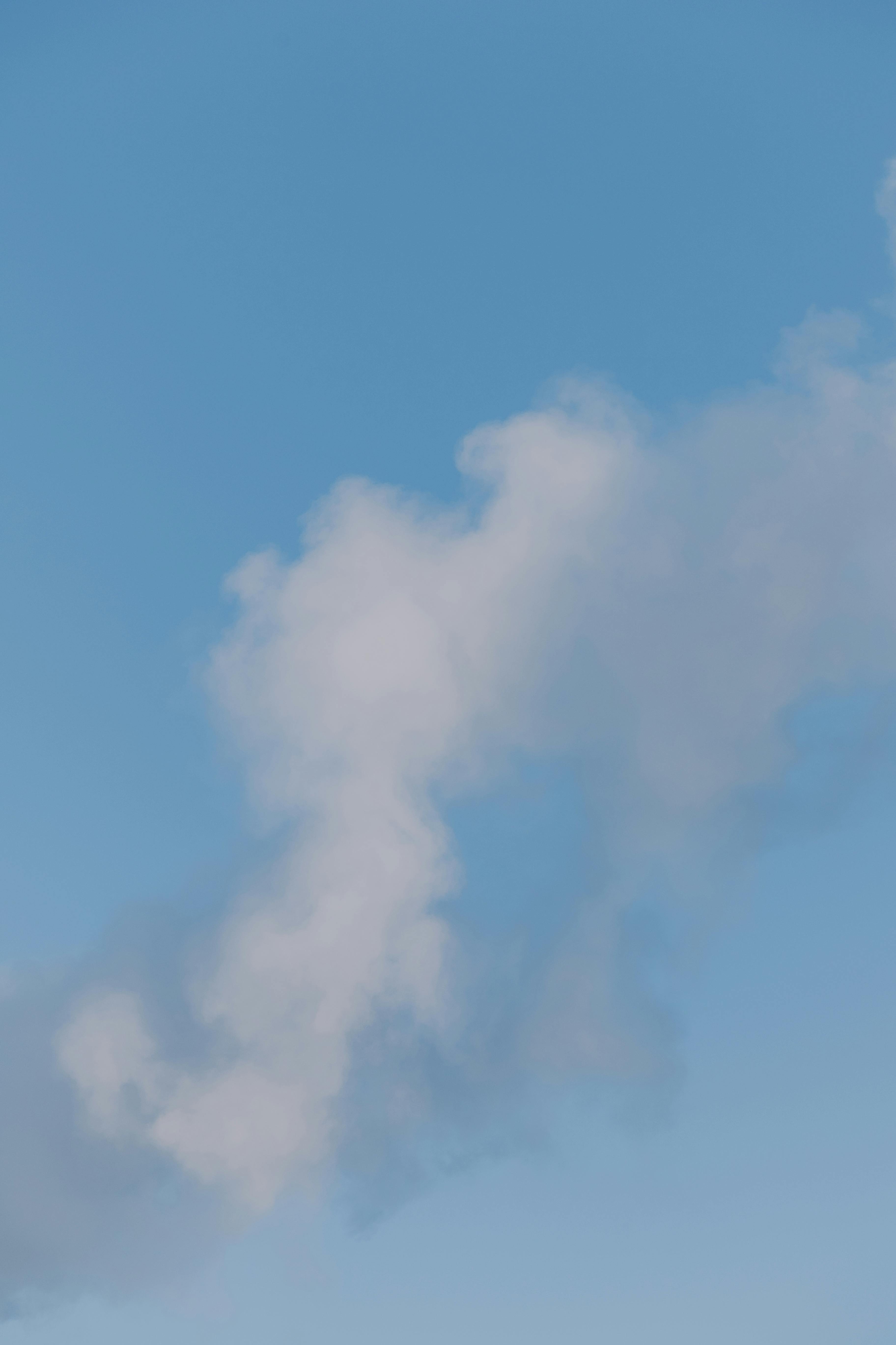 Free A delicate, wispy cloud floats in a clear blue sky, capturing a serene moment. Stock Photo