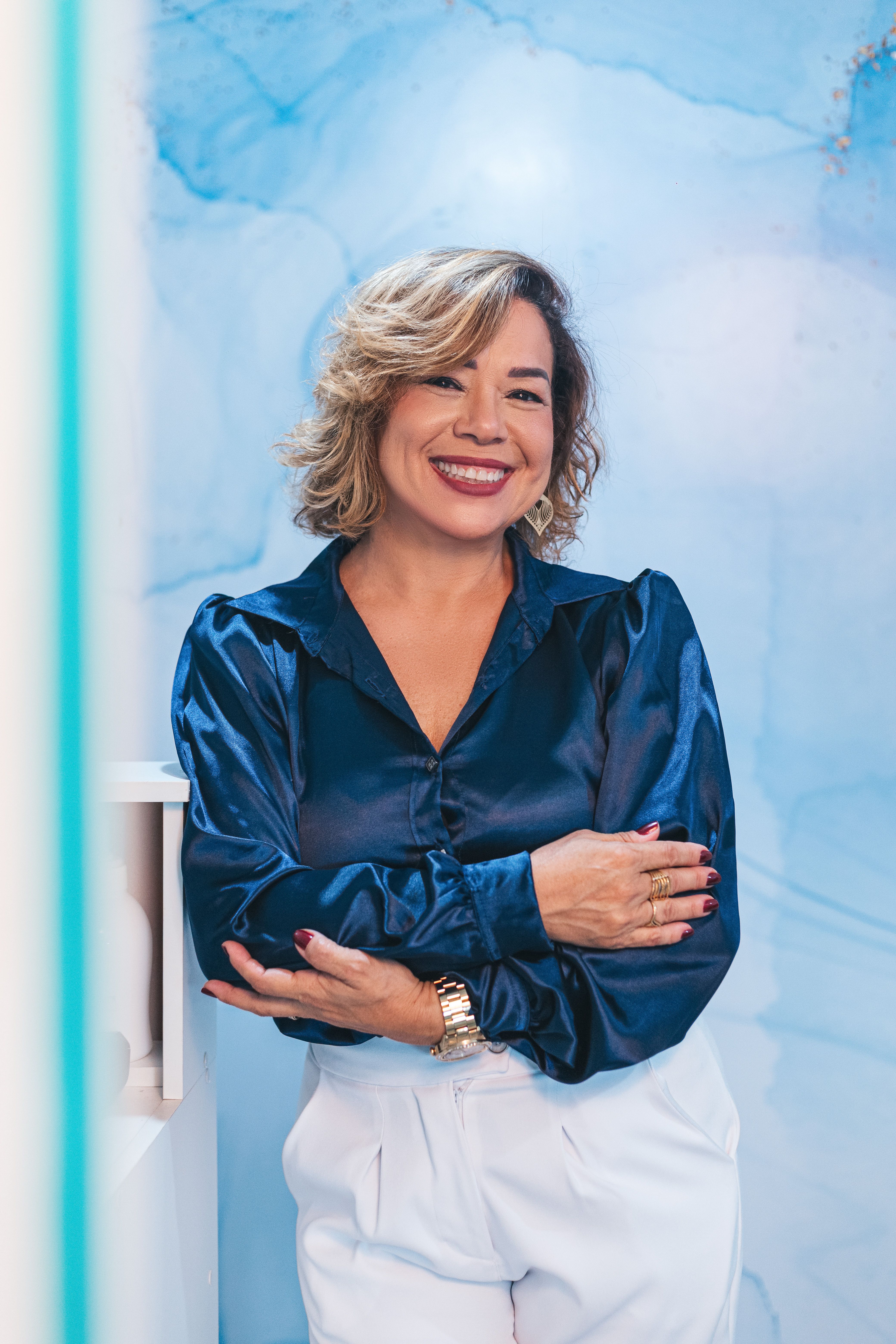 Elegant woman smiling confidently in a blue blouse against artistic backdrop.