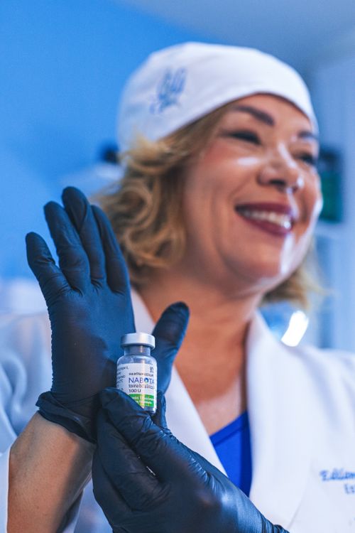 Free Smiling healthcare worker holding a vaccine vial labeled NAOBOT in a clinic setting. Stock Photo