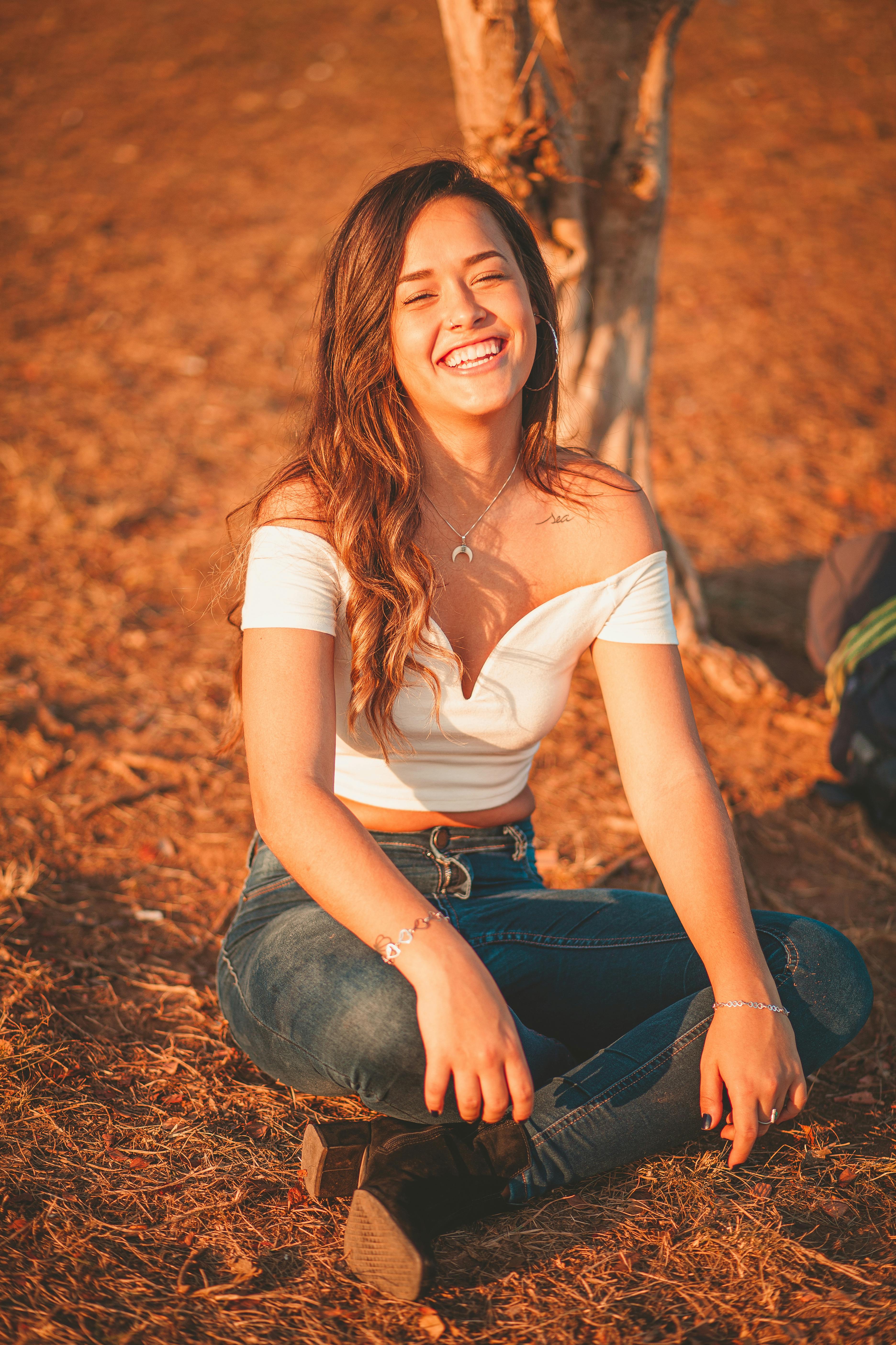 温暖的阳光下，一位穿着休闲装的年轻女子坐在草地上，笑容灿烂