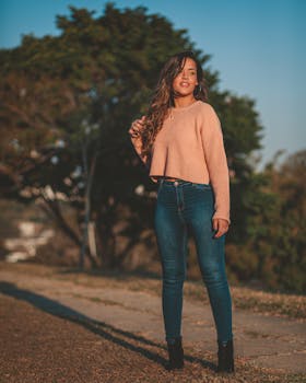 时尚女性穿着牛仔裤和毛衣在户外，展现出自信与休闲的风格