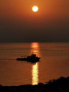 A boat silhouette during a picturesque sunset over calm waters, creating a serene scene.