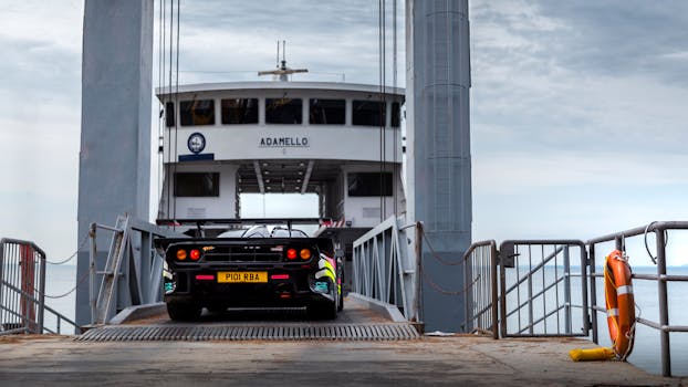A McLaren supercar driving onto a ferry named Adamello in the scenic Italian Alps.