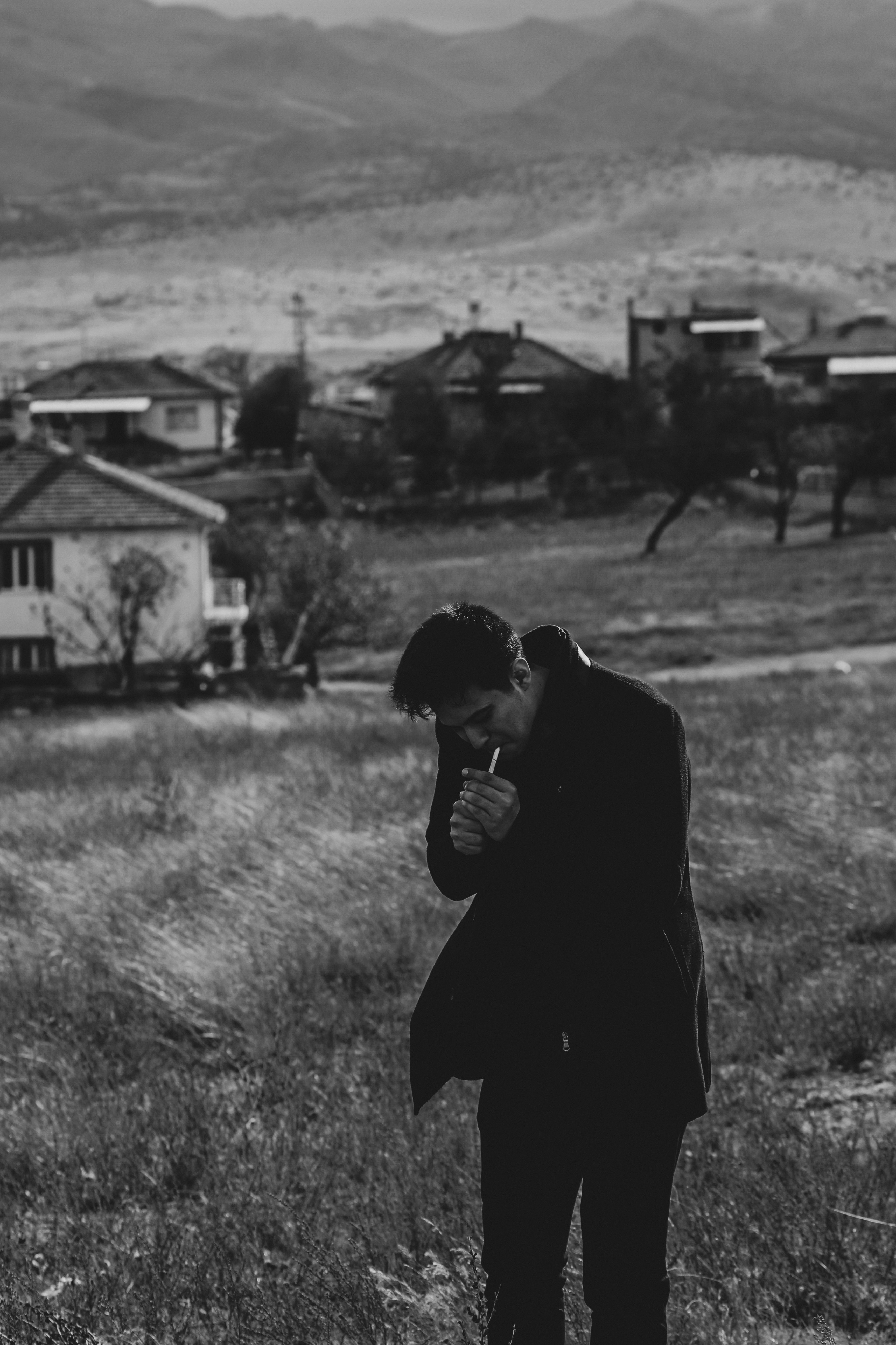 Moody black and white portrait of a man in a rural village setting with mountains.