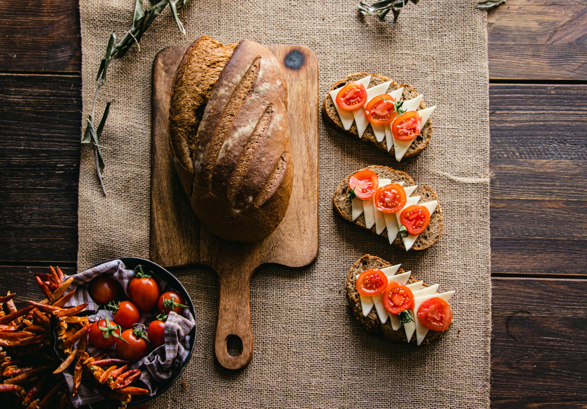 Top view of a rustic bread loaf with cheese and tomato slices on wooden table.