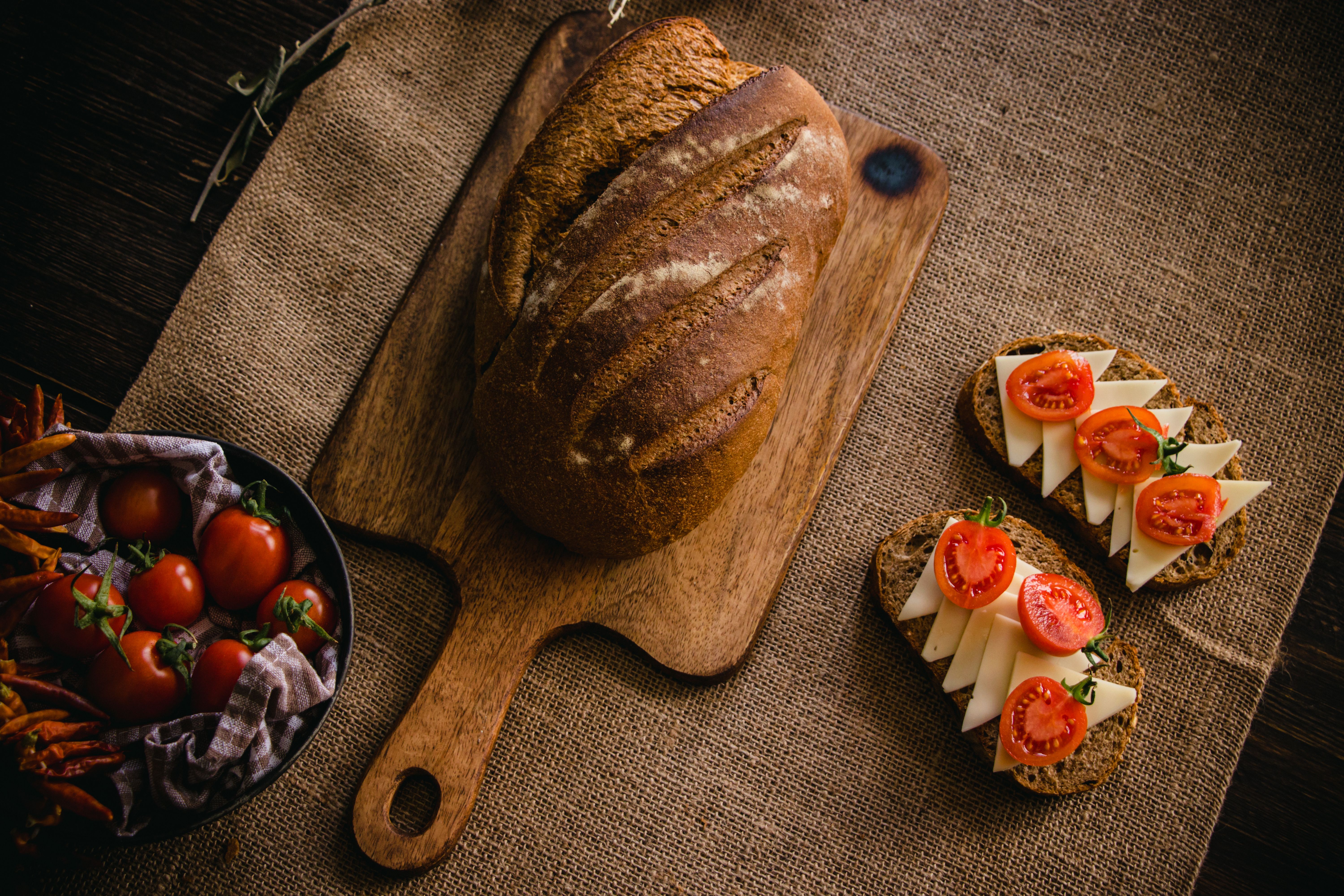 Artisan bread on a cutting board with cheese and tomato slices on burlap cloth. - Photo by Beyza Yalçın on Pexels