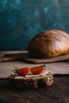 Close-up of rustic bread topped with cheese and cherry tomatoes on a dark wooden table.
