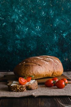 Rustic loaf and cherry tomatoes on wooden board for a cozy dinner setup.